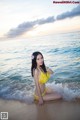 A woman in a yellow bikini sitting on the beach.