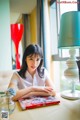 A woman sitting at a table with a book and a lamp.