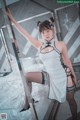 A woman in a white dress and black stockings posing on a bed.
