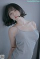 A woman in a gray tank top leaning against a wall.