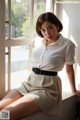 A woman sitting on a window sill wearing a white shirt and skirt.