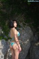 A woman in a blue bikini standing on a rock.