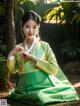 A woman in a green and yellow hanbok sitting on the ground.