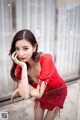 A woman in a red dress leaning against a glass railing.