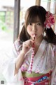 A woman in a kimono holding a lollipop in her mouth.