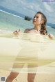 A woman standing on a beach holding a yellow scarf.