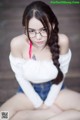 A woman wearing glasses sitting on a wooden floor.