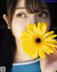 A woman holding a yellow flower in front of her face.